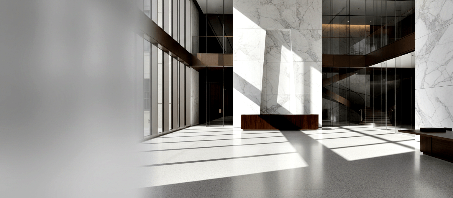 Multi-story lobby atrium with dark wood reception desk, marble columns, glass-railed staircase, and geometric shadows on polished gray floor.