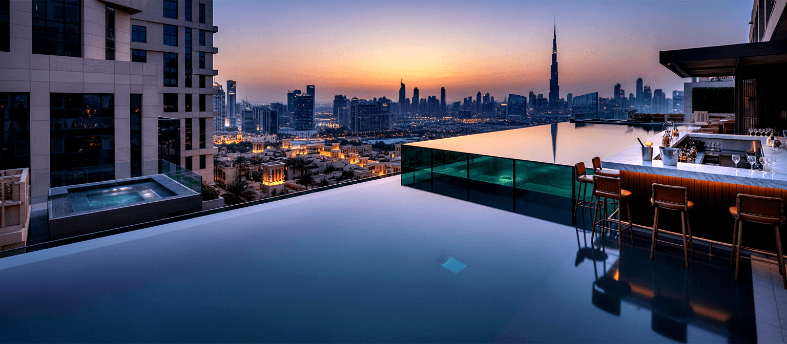 Rooftop infinity pool with glass sides and teal-lit water, marble bar with leather stools, illuminated cityscape under twilight sky.