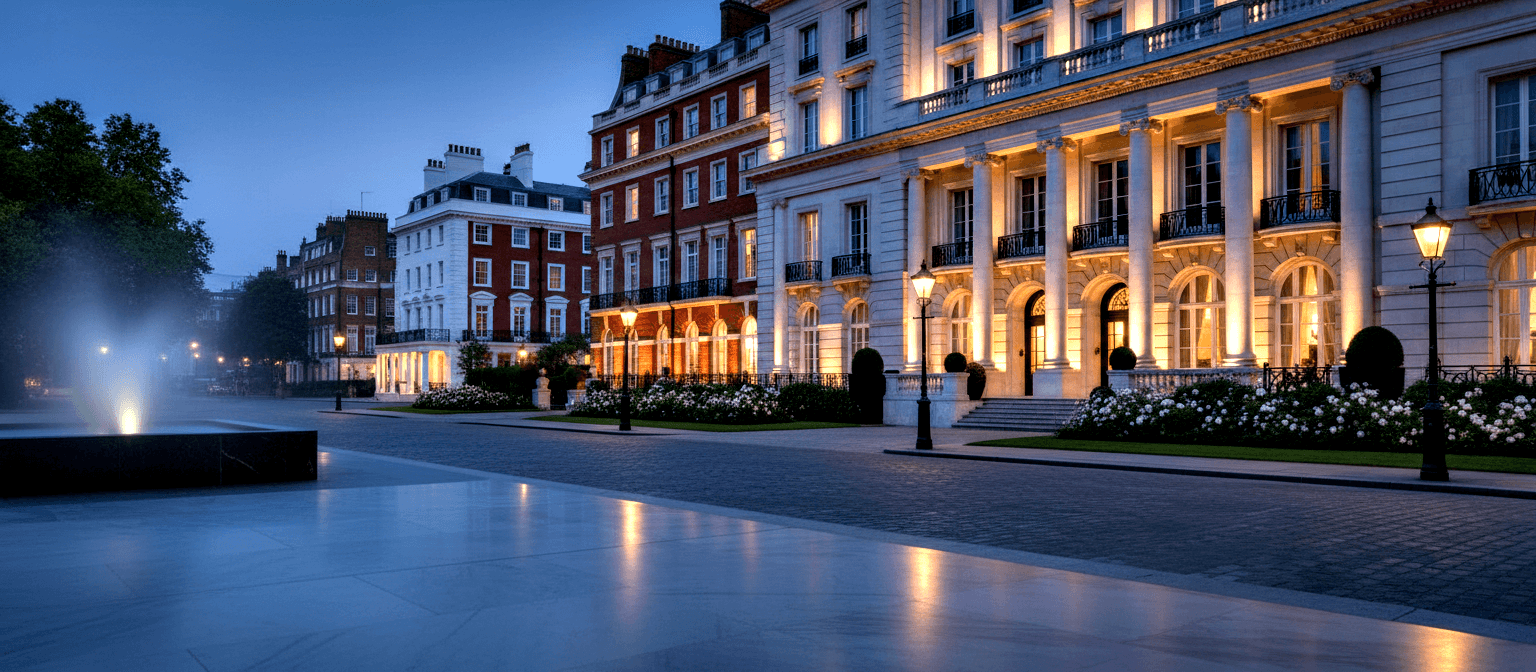 Neoclassical stone building with tall columns and iron balcony railings, amber-lit at dusk against deep blue twilight sky.