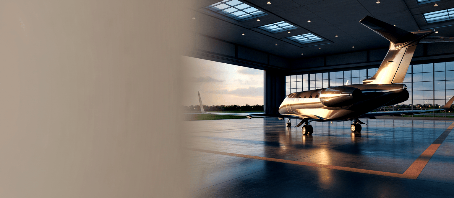 Dark charcoal business jet in a modern hangar with polished floor, orange-red border lines, and warm spotlights.