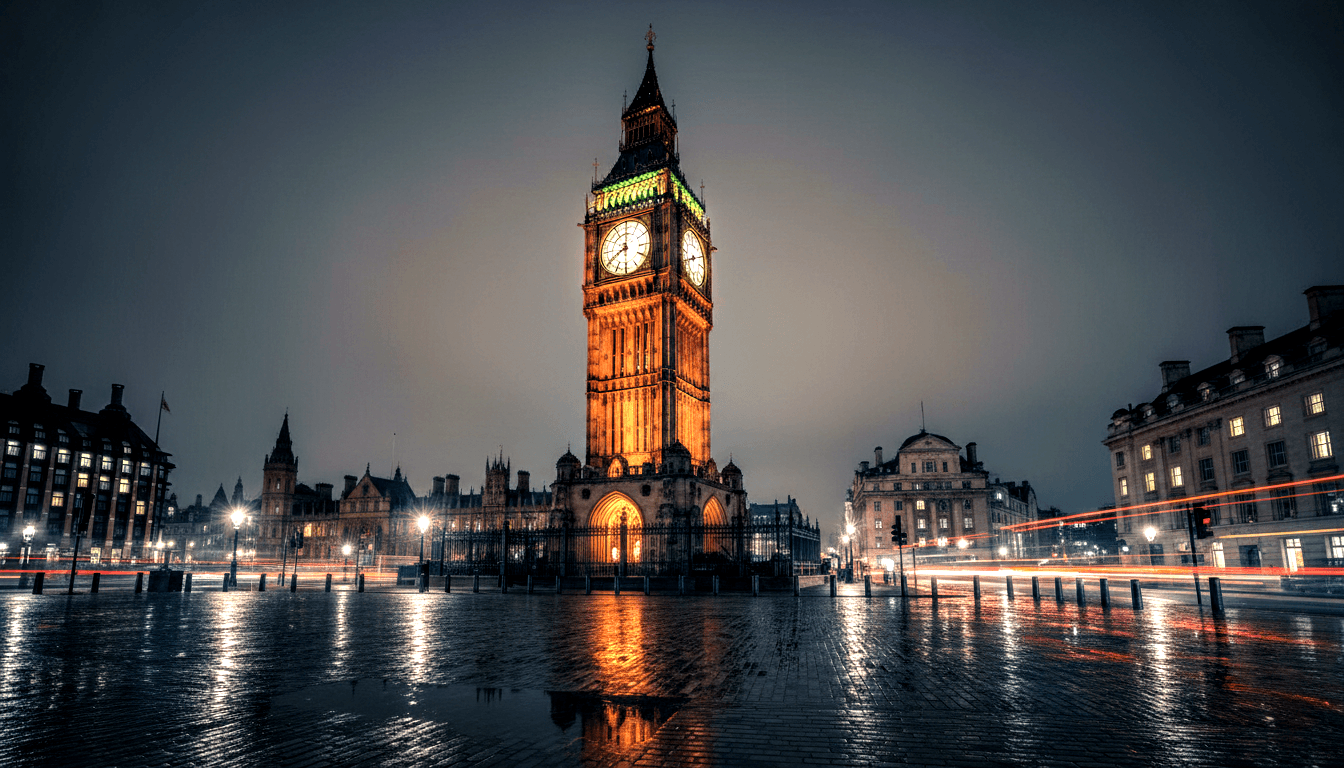 Tall Gothic clock tower with four glowing amber faces, floodlit at night, reflected in rain-slicked cobblestones below.
