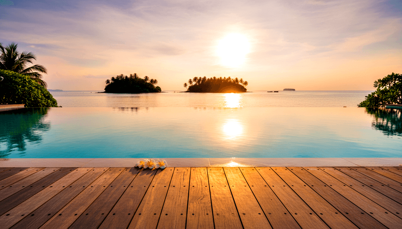 Infinity pool with turquoise water merging into calm ocean at sunset, three white plumeria flowers on ledge, palm-covered island silhouettes.