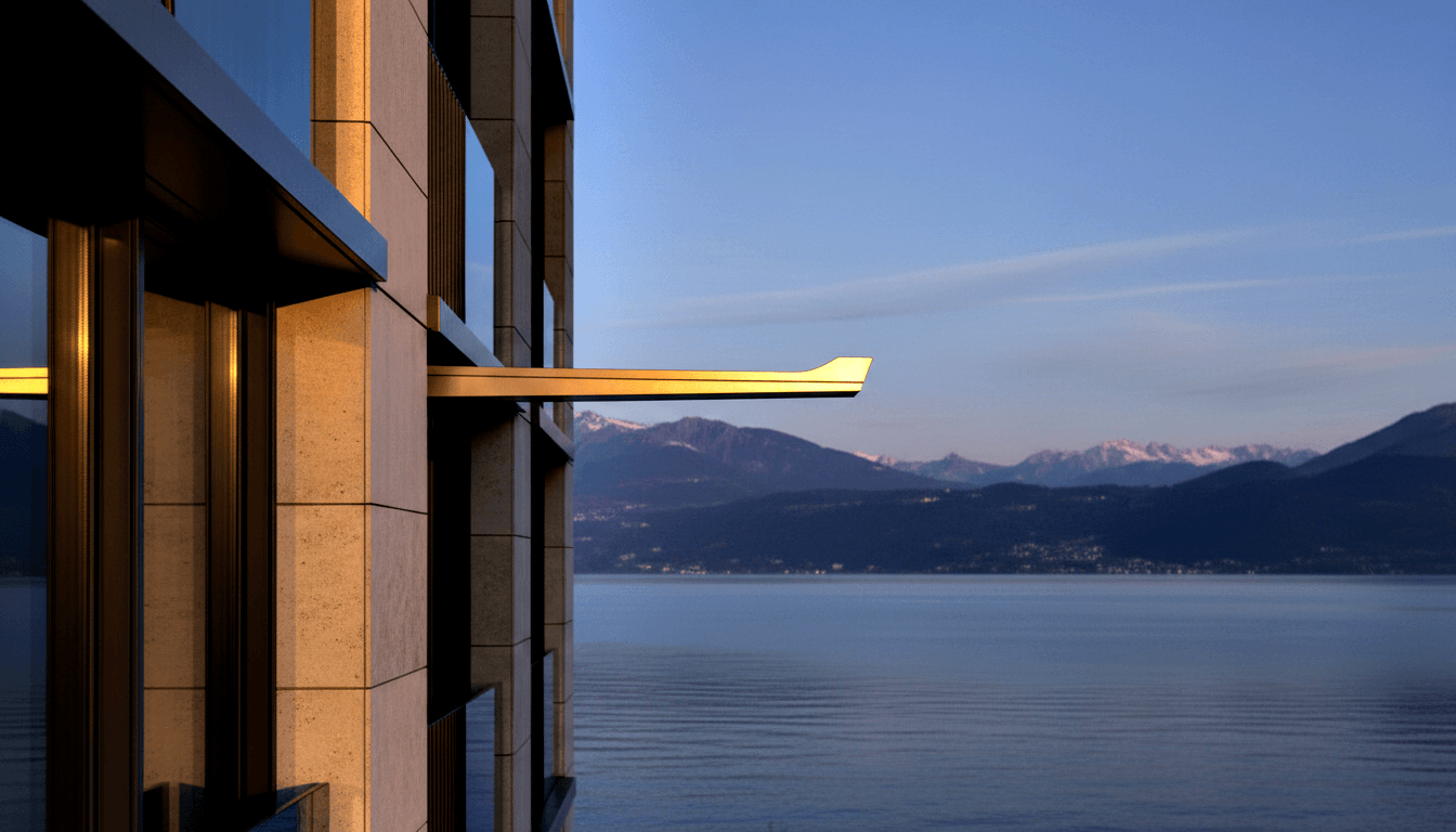 Stone-clad building with travertine facade and cantilevered balcony beside a calm alpine lake reflecting snow-capped peaks at dusk.