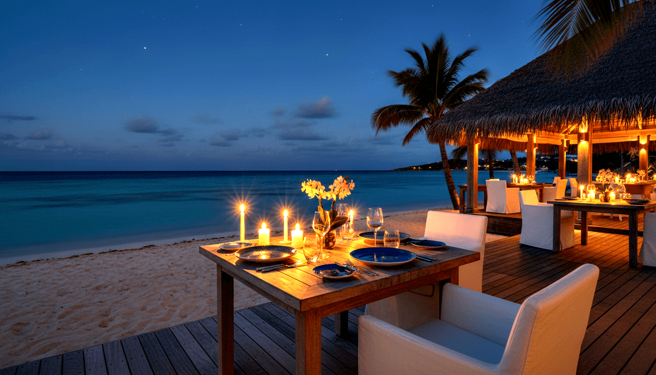 Outdoor beachfront dinner table for two with blue plates, wine glasses, candles, and yellow orchid centerpiece at twilight.